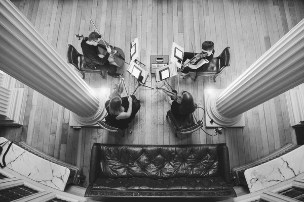 String quartet from above — four violinists and a cellist in black, ready to perform