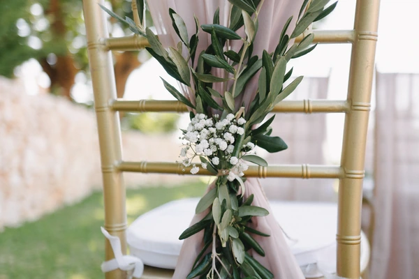 Bamboo chair decorated with olive branches, white gypsophila and pastel ribbon at the ceremony venue