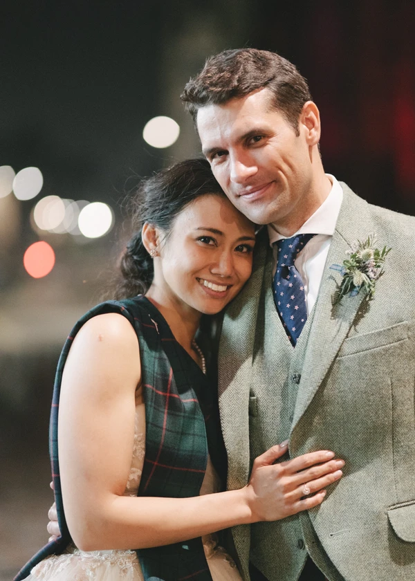 Happy newlywed night portrait — both smiling close together, city lights behind