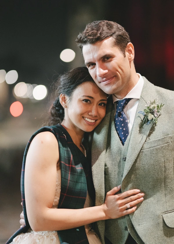 Happy newlywed night portrait — both smiling close together, city lights behind