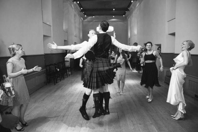 Ceilidh dancing in the Edinburgh Castle, black and white documentary photograph of the groom and groomsmen dancing it a wedding