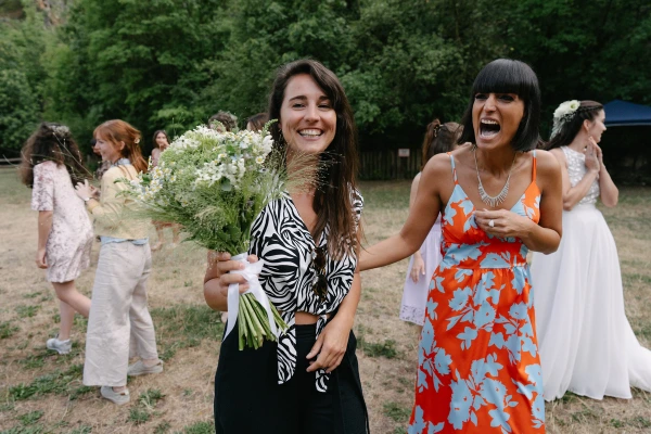 Two women smiling holding daisy bouquet together at outdoor garden wedding celebration event.