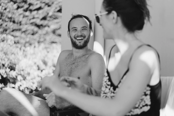 Couple laughing together by a white flower-decorated room — groom with radiant smile. Black-and-white.