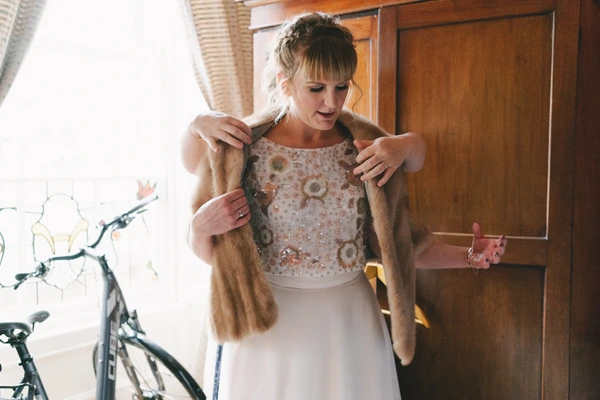 Bride in beige cardigan models her sparkling top and white skirt at home, cheerful expression