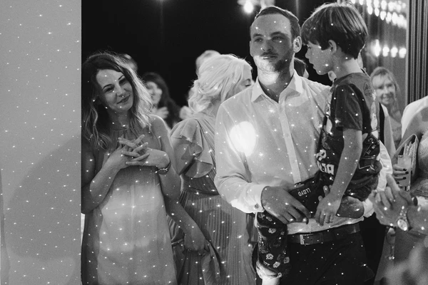 Wedding guests by the dance floor — black-and-white, man in white shirt, elegant dress, glittering backdrop