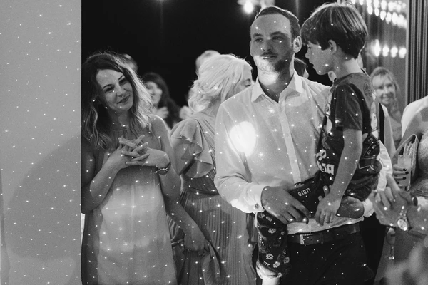 Wedding guests by the dance floor — black-and-white, man in white shirt, elegant dress, glittering backdrop