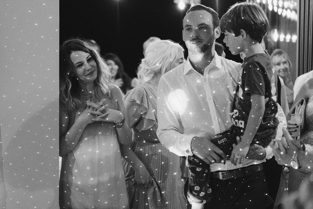 Wedding guests by the dance floor — black-and-white, man in white shirt, elegant dress, glittering backdrop