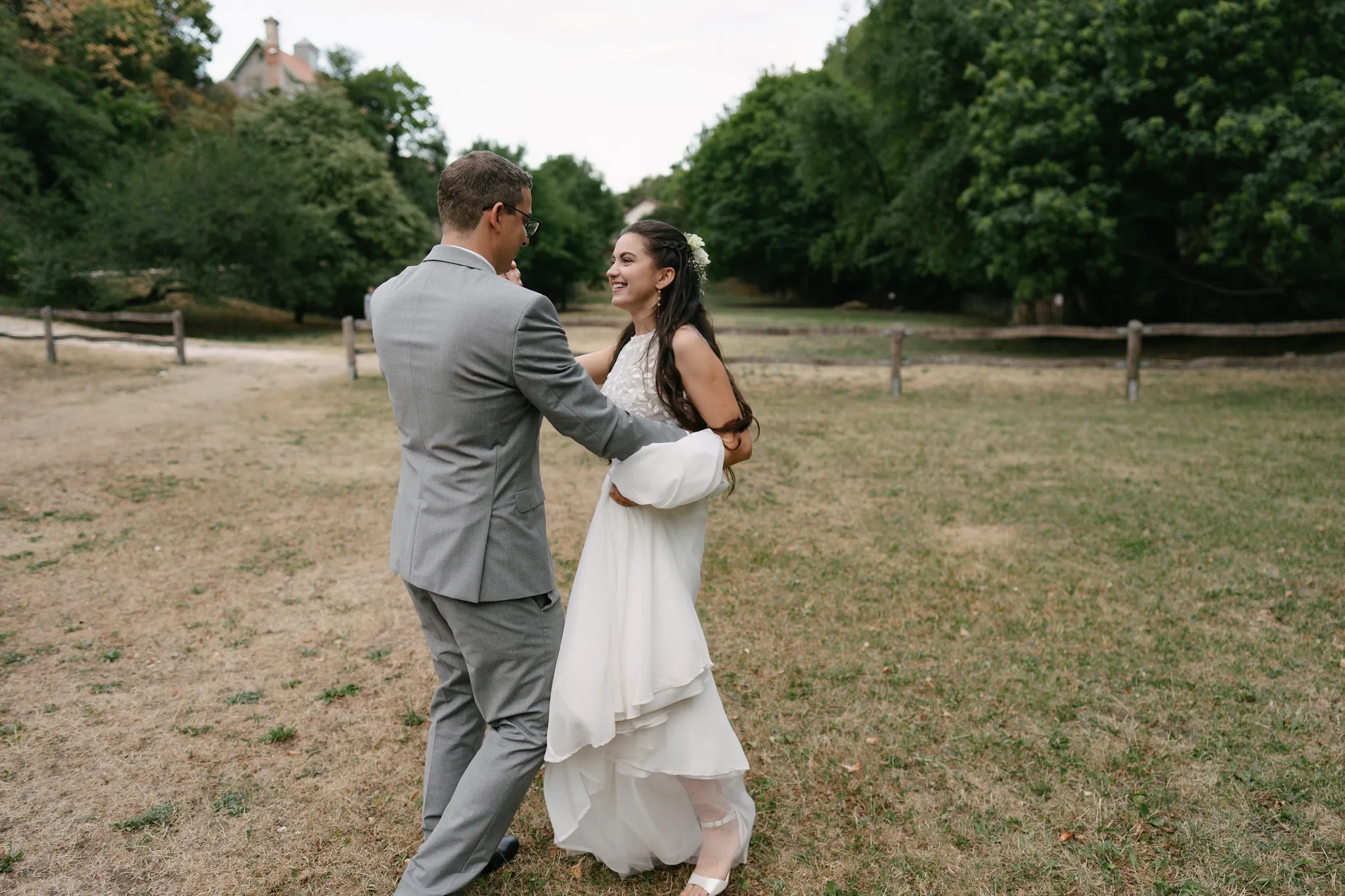Bride and groom dancing in open field surrounded by trees during outdoor wedding reception