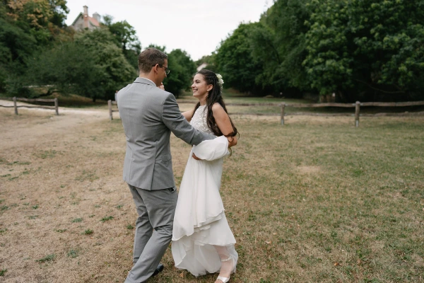 Newlyweds walking and holding hands at outdoor wedding ceremony with green trees and natural venue.