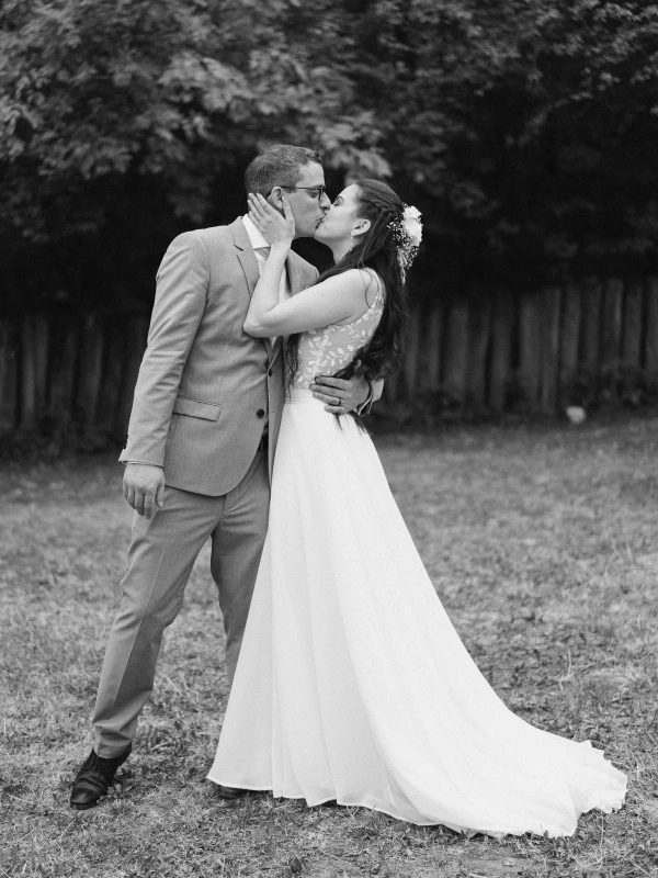 Black and white romantic photo of bride and groom kissing with white dress and suit at wedding.