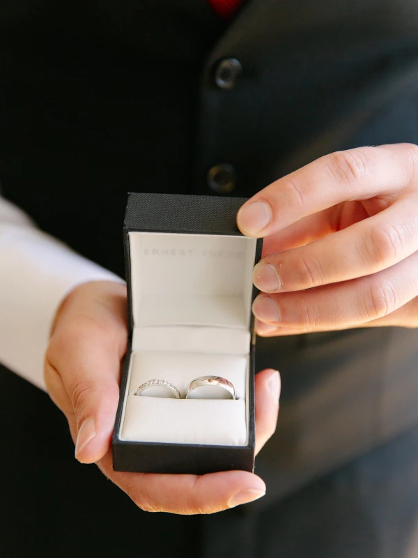 Best man holding open a black ring box containing two platinum wedding bands. Close-up detail shot before the ceremony.