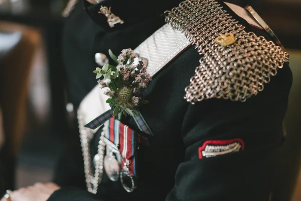 Groom in ceremonial military uniform holds the bridal bouquet detail with white gloves