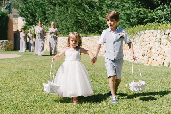 Two children with flower basket walk in the garden at the wedding — bride and father in background