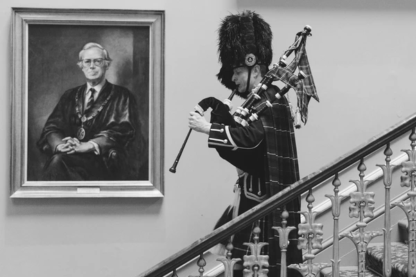 Scottish piper on the staircase in full regalia — black uniform, bearskin hat, tartan kilt