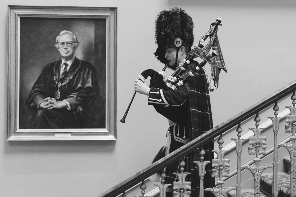 Scottish piper on the staircase in full regalia — black uniform, bearskin hat, tartan kilt