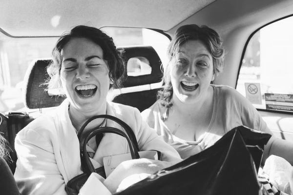 Two women laughing inside a car — black-and-white, natural sunlight through the windows