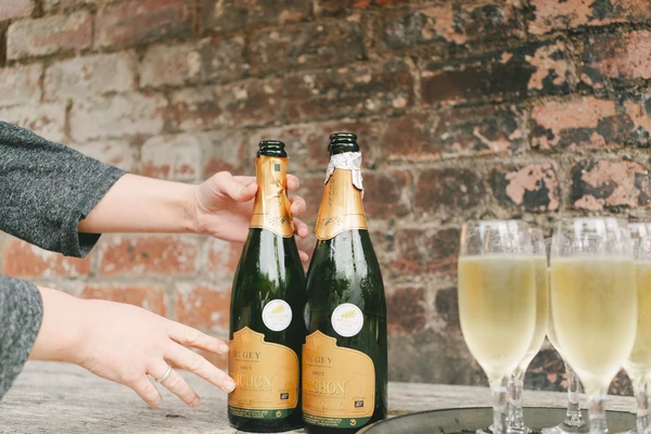 A couple's hands clasped over two champagne bottles on a cobblestone background