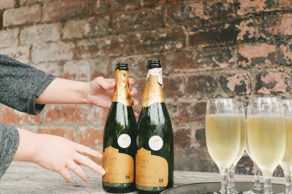A couple's hands clasped over two champagne bottles on a cobblestone background