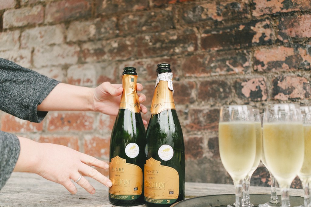 A couple's hands clasped over two champagne bottles on a cobblestone background