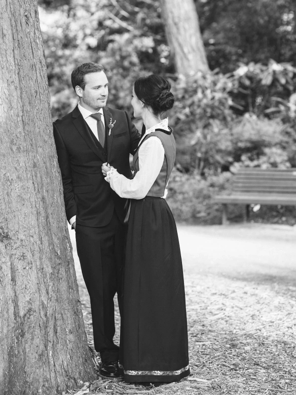 Black and white image of the bride and groom standing close together by a tree, holding hands and facing each other tenderly. Documentary wedding portrait at the Royal Botanic Garden Edinburgh.
