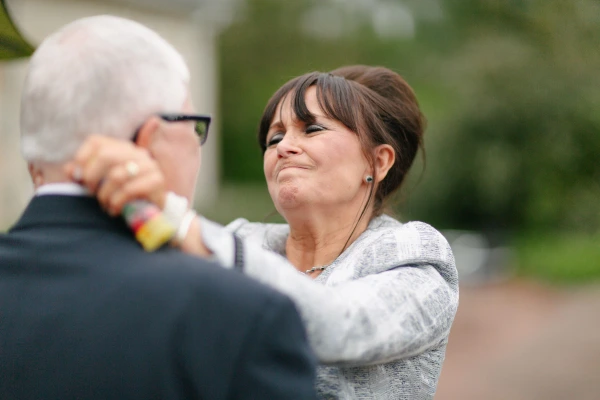 A woman pulls a bittersweet emotional expression while looking at an older man with glasses at the wedding reception. Candid and tender documentary moment.