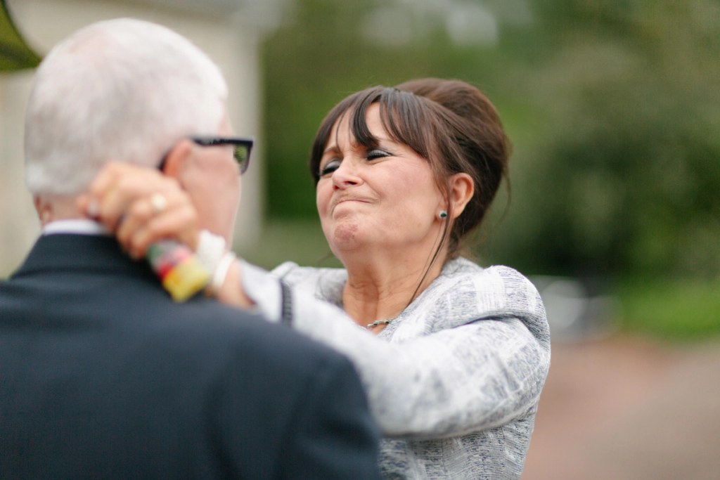 A woman pulls a bittersweet emotional expression while looking at an older man with glasses at the wedding reception. Candid and tender documentary moment.