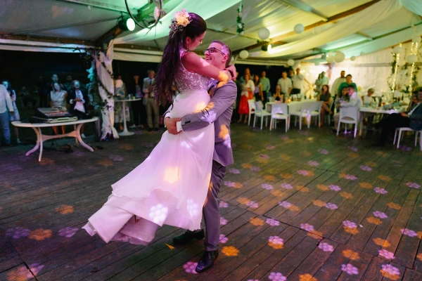 Bride and groom dancing under tent at evening wedding reception with colorful uplighting.
