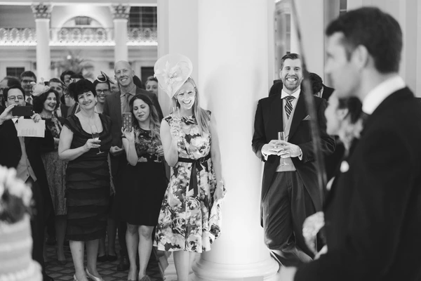 Wedding guests smile and watch the groom with a woman in white in an elegant colonnade — black-and-white