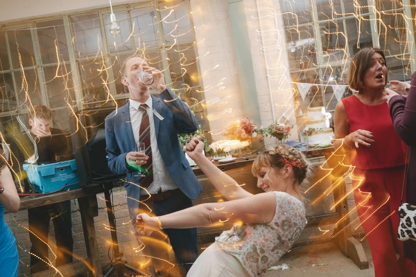 Bride and groom dance joyfully among guests amid golden fairy lights in the wedding hall