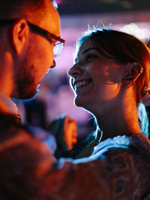 Bride and groom laugh together at evening reception — neon-lit atmosphere, intimate couple moment, warm orange and blue tones.