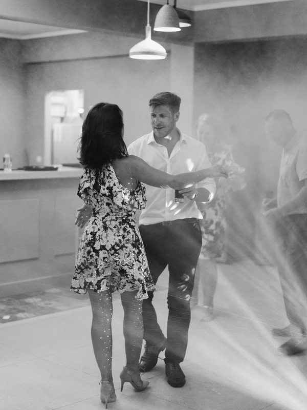 Couple dances at the reception — man in white shirt, woman in floral dress, pendant light above them