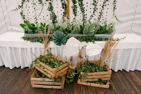 Wedding reception decor featuring wooden crates filled with ivy and paper fans under a white tent.