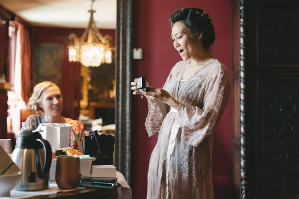 Woman in white lace robe holds a gift box, smiling — warm golden light, red walls