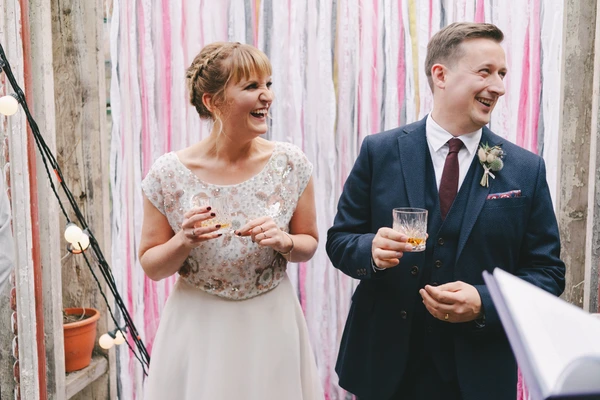 Bride and groom laughing together, holding drinks at the wedding celebration