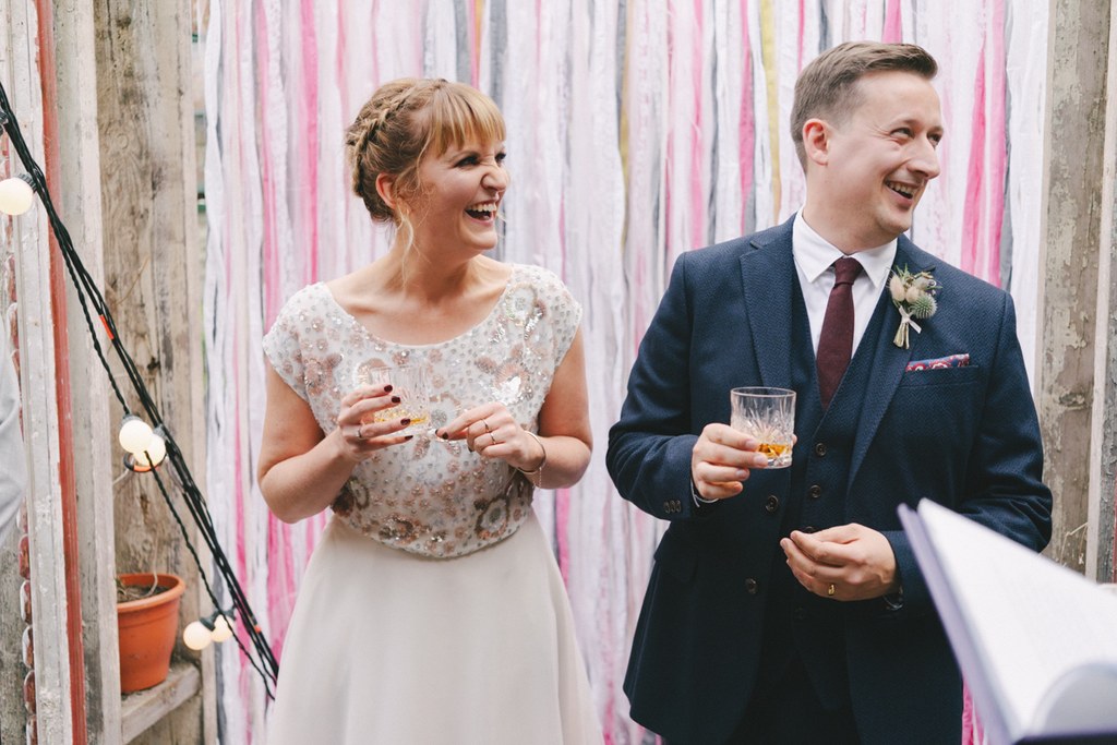 Bride and groom laughing together, holding drinks at the wedding celebration