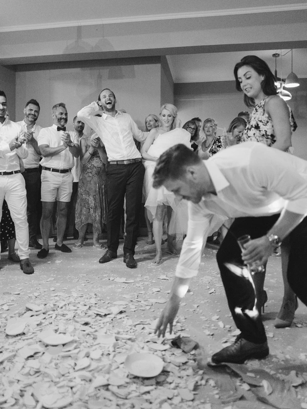 Wedding guests laughing as groom falls into the sand at the party — black-and-white