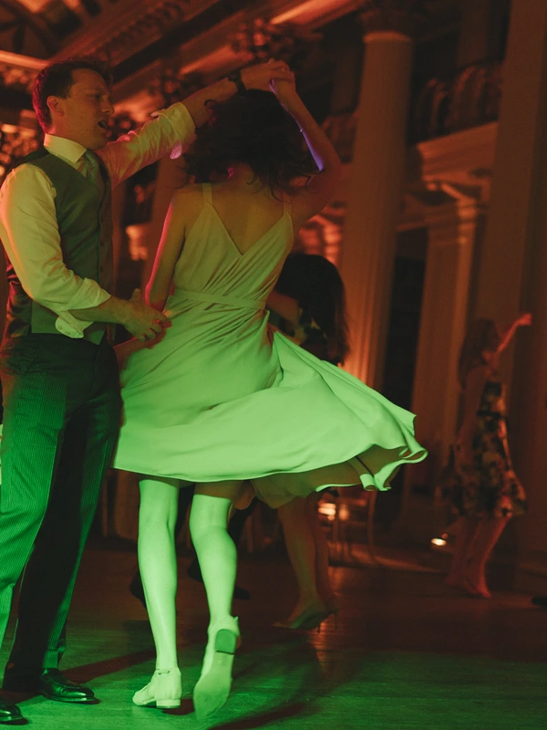 Couple dances at the reception in vivid green and orange laser light — woman in pale green spins