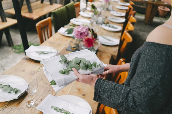 Guest holds a eucalyptus branch on a napkin beside a flower-decorated wedding feast table