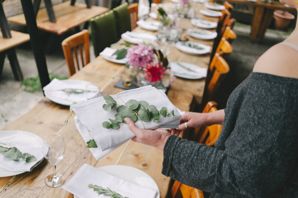 Guest holds a eucalyptus branch on a napkin beside a flower-decorated wedding feast table