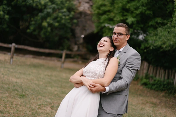 Bride and groom dancing together joyfully at outdoor wedding with green nature background scenery.