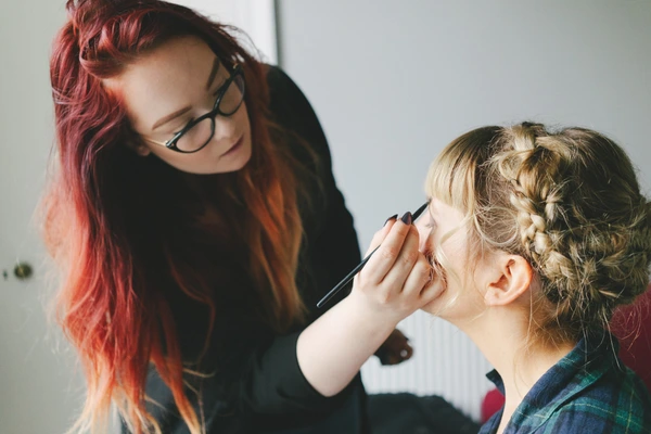 Makeup artist with glasses works on the bride's bare face before the ceremony