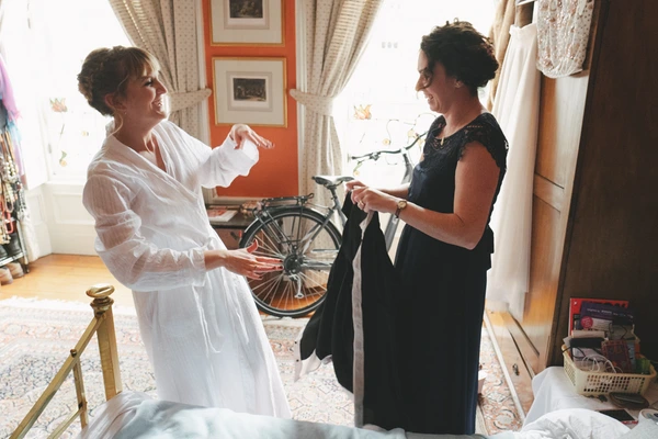 Bride in white dress and a woman in black chat cheerfully in a vintage room with a bicycle