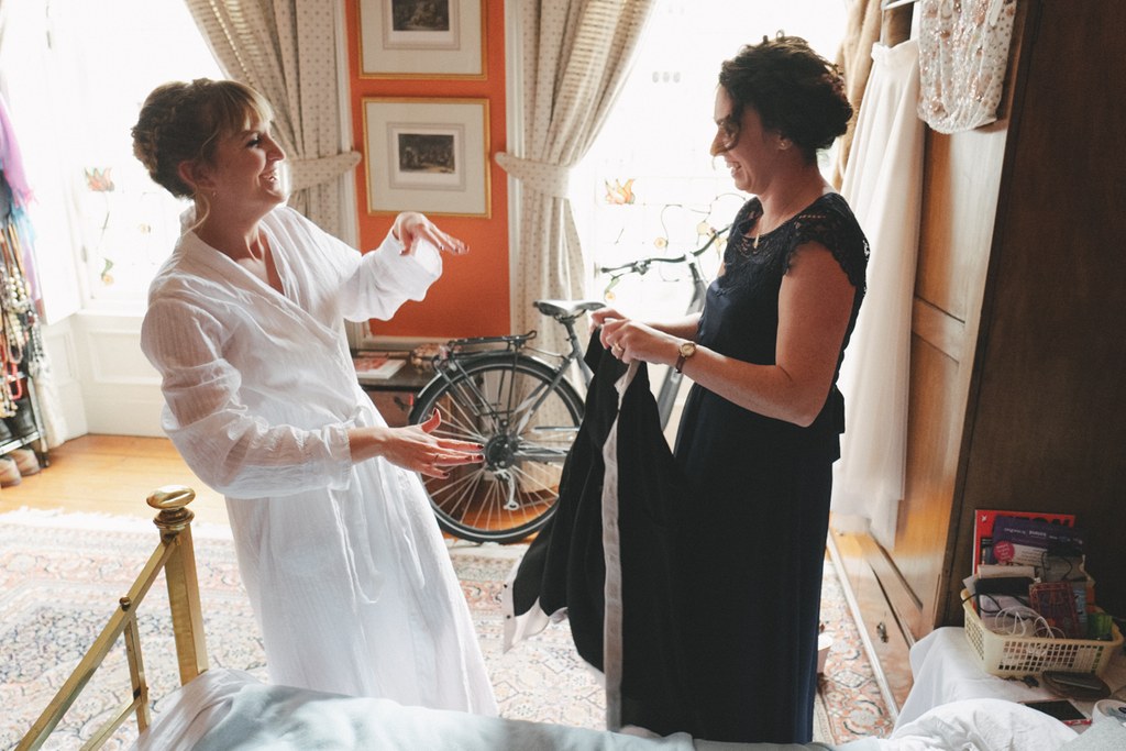 Bride in white dress and a woman in black chat cheerfully in a vintage room with a bicycle