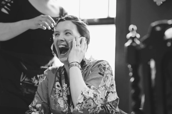 Woman in floral robe laughing on the phone while someone styles her hair — black-and-white