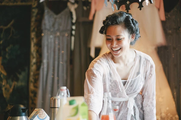 Young bride in white lace smiling broadly at the table — warm golden light, drinks and food around