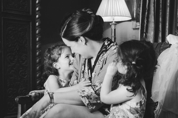 Mother in floral dress plays with three smiling children in an elegant room — black-and-white