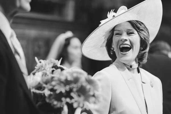 Elegant woman in white hat and coat laughing with her bouquet at the wedding — genuine joy