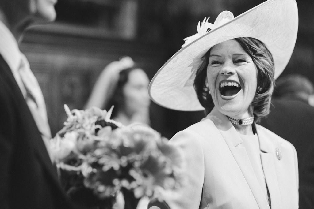 Elegant woman in white hat and coat laughing with her bouquet at the wedding — genuine joy
