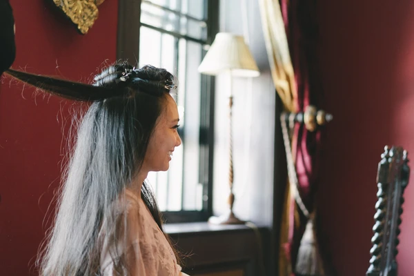 Bride in profile with a long white veil and floral hair piece, natural light flooding her face