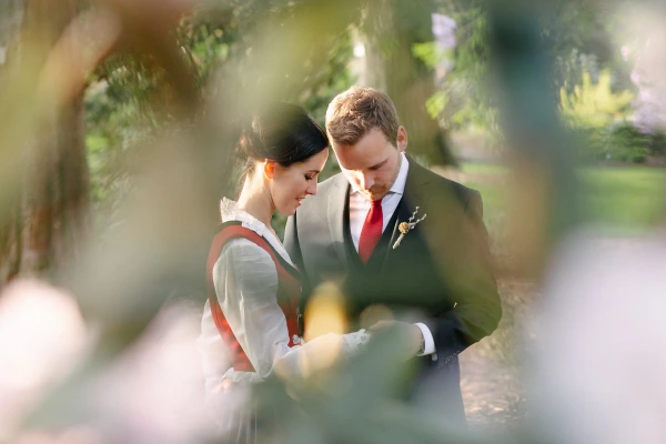 The bride and groom are photographed through foliage in warm golden light, foreheads close together in a private, tender moment. Documentary wedding portrait at the Royal Botanic Garden Edinburgh.